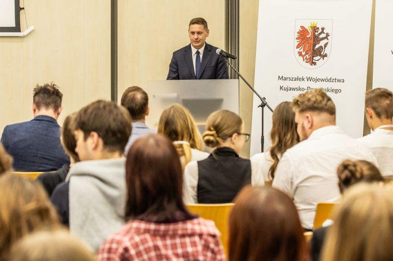 Publiczność patrząca na mężczyznę przemawiającego przy mównicy