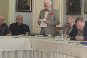 Osoba przemawiająca, pozostałe osoby siedzą za stołem